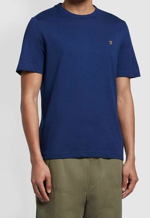 T-shirt in cotone blu navy con maniche corte, collo rotondo e piccolo logo ricamato sul lato sinistro del petto, abbinato a pantaloni verdi oliva.