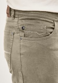 Olive green trousers made of soft cotton blend. Features two back pockets, white stitching, and a small label on the front pocket.