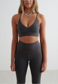 Gray sports bra with a V-neck design and thin straps, paired with high-waisted gray leggings, both made of smooth, stretchy material.