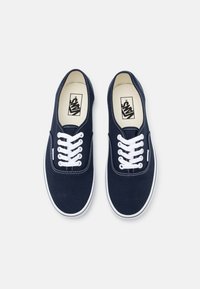 Marinblå canvas sneakers med vita snören, rundad tå och vita gummisulor. Har kontrasterande sömmar och en logotyp på tungan.