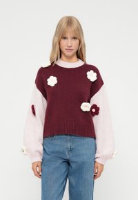 Pulover tricotat burgund și roz cu aplicații florale. Croială boxy, mâneci lungi și puffate, tiv cu nervuri. Material moale, texturat. Culori luminoase.
