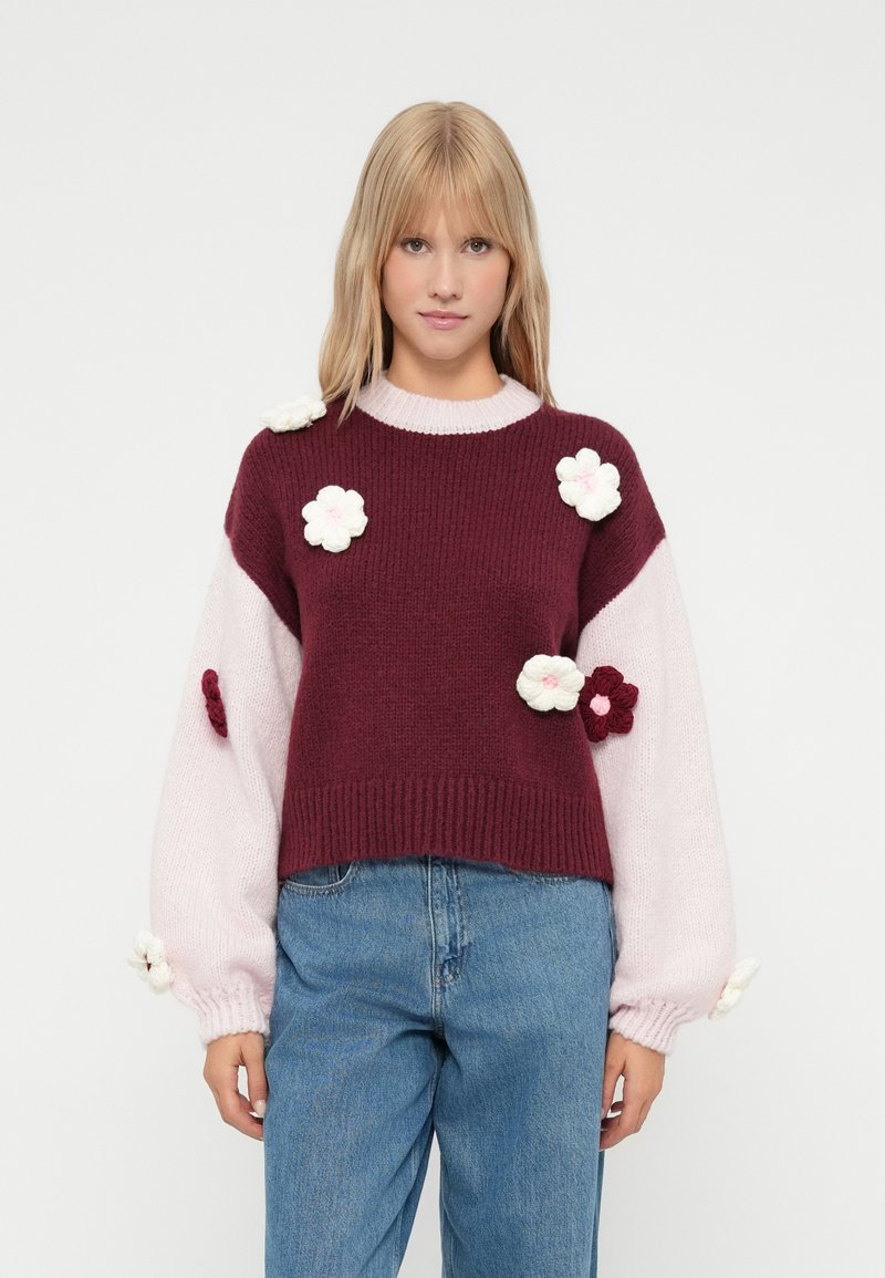 Pulover tricotat burgund și roz cu aplicații florale. Croială boxy, mâneci lungi și puffate, tiv cu nervuri. Material moale, texturat. Culori luminoase.