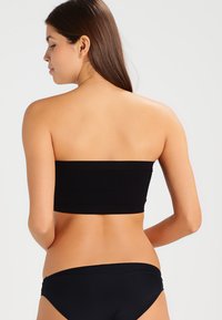 Haut noir sans bretelles en tissu lisse et extensible. L'arrière est uni avec un design sans couture, associé à un bas de bikini noir taille basse.