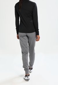 Czarna dopasowana bluzka z długim rękawem w połączeniu z szarymi spodniami dresowymi. Strój cechuje się gładką fakturą oraz sportowym obuwiem z czarno-białymi akcentami.