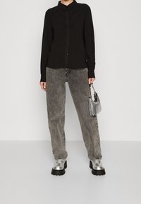Black button-up shirt with textured stitching, paired with gray high-waisted jeans and silver platform shoes. Accessories include a small metallic bag.