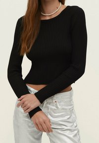 Top court noir côtelé à manches longues avec un col rond, associé à un pantalon argenté brillant. Le haut présente une coupe ajustée et un tissu texturé.