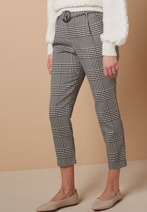 Pantalons à carreaux noir et blanc au design ajusté, avec une ceinture à la taille et une longueur cropped, associés à des ballerines beige clair.