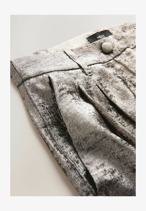 Pantaloni plisati metalici argintii cu textură moale, având detalii la nasturele din față și la talie, expuși dintr-un unghi. Eticheta brandului este vizibilă.