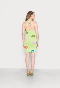 Robe en tricot verte avec de grands motifs floraux multicolores, décolleté halter et design ajusté. Associée à des talons verts à lanières.