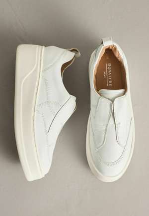 White leather slip-on shoes with a round toe, textured surface, contrasting stitching, and a white rubber sole. Features a pull tab at the heel.