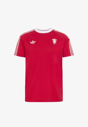 Camiseta roja de Adidas con tres franjas blancas en las mangas, cuello redondo blanco, logo del trébol de Adidas y un pequeño gráfico blanco de un león sosteniendo un tridente.