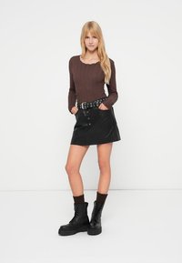 Καφέ μακρυμάνικη πλεκτή μπλούζα, μαύρη φούστα Α-γραμμής από δερματίνη με κουμπιά, μαύρα μποτάκια τύπου combat και καφέ πλεκτές κάλτσες.