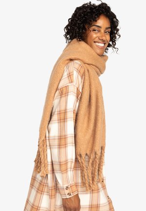 Gran bufanda oversized de material suave y texturizado, con flecos en los extremos. Se lleva drapeada sobre los hombros.