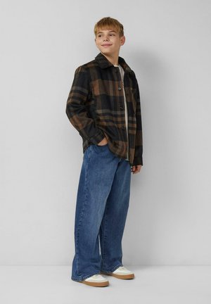 Brązowo-czarna koszula flanelowa w kratę, zapinana na guziki, z kołnierzykiem. Nosi się ją na jasną koszulę, w zestawie z luźnymi niebieskimi dżinsami i kremowymi trampkami.