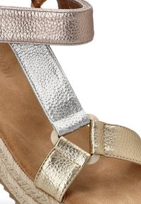 Sandalias metálicas con hebillas en plata, oro y oro rosa, un acabado texturizado y una plantilla de color natural con un detalle en forma de círculo.