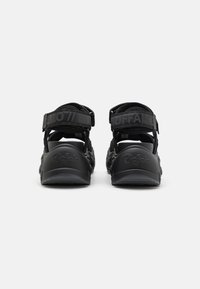 Sandales noires au design ouvert, dotées de brides réglables et d'une semelle texturée. Le logo embossé sur le talon et la bride apporte une touche de marque.
