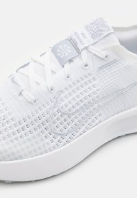 Pantoflă sportivă albă cu un superior din plasă texturată, față cu șireturi, guler căptușit și talpă din cauciuc. Prezintă un cod QR pe eticheta de la limbă.