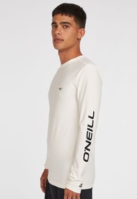 Biała rash guard z długim rękawem, wykonana z elastycznego materiału, z czarnym logo O'Neill na lewym rękawie oraz małym logo na klatce piersiowej.