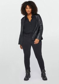 Blazer de cuero negro sobre una camisa de botones negra, combinado con pantalones negros con acentos de tachuelas en los puños. Botines negros.