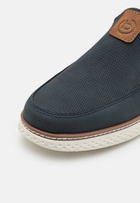 Chaussure bleu marine avec une tige en textile texturé, accent en cuir marron et semelle blanche à motif. Bout rond et détails cousus.