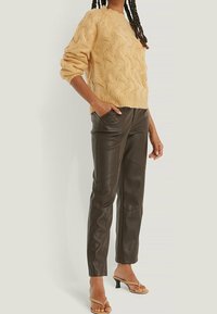 Pull en maille torsadée crème avec ourlet côtelé, associé à un pantalon en cuir marron avec une finition lisse et des coutures ajustées. Des talons beiges à lanières complètent le look.