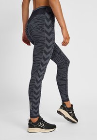 Högmidjade leggings i mörk marinblått med ett strukturerat zickzackmönster. Materialen ser ut att vara stretchy och andas. Bärs med svarta sneakers.