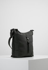 Sac en cuir noir à bandoulière avec un design décontracté, doté de quincaillerie en argent, d'une poche zippée à l'avant et d'une bandoulière détachable.