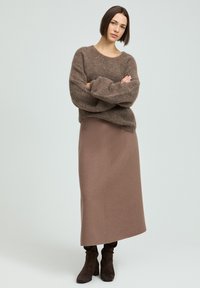 Brauner, flauschiger Strickpullover mit Rundhalsausschnitt, kombiniert mit einem langen, figurbetonten, hellbraunen Rock. Gestylt mit dunklen Stiefeln bis zur Knöchel.