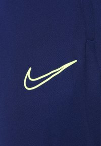 Marineblauwe stof met een gladde textuur en een opvallend, reflecterend geel Nike Swoosh-logo. Eenvoudig ontwerp, geen extra details.