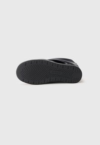 Semelle de chaussure en caoutchouc noire avec un motif en chevrons, présentant un logo en relief et une forme courbée. Texturée pour une meilleure adhérence et durabilité.