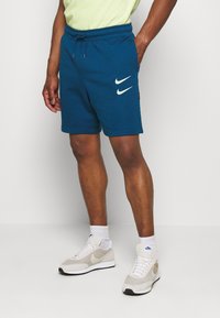 Blue cotton shorts with an elastic waistband and drawstring, featuring two white Nike logos on the left leg and side pockets.