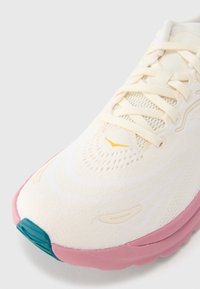 Αθλητικό παπούτσι σε ανοιχτ ό κρέμ με ροζ σόλα. Διαθέτει επάνω μέρος από δίχτυ, επίπεδα κορδόνια και πετρόλ κορυφή δακτύλων. Λεπτή υφή και μινιμαλιστικές λεπτομέρειες σχεδίασης.