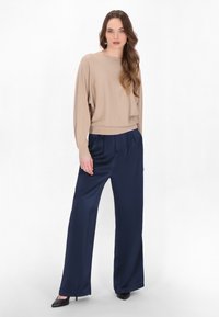 Beige, metalen gebreide top met lange mouwen, gecombineerd met marineblauwe satijnen broek met wijd flanellen en zwarte hoge hakken. Zachte texturen en een relaxte fit.