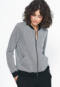 Czarno-biała bomberka z zamkiem błyskawicznym w wzór rybiej ości, z prążkowanym kołnierzem i mankietami, posiadająca dwie przednie kieszenie oraz fakturowany materiał.