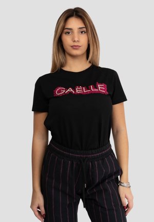 T-shirt nera con lettering "GAELLE" rosso testurizzato sulla parte anteriore. Maniche corte, collo rotondo, abbinata a pantaloni neri a righe.