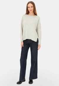 Jasnoszary, oversize sweter z prążkowanymi mankietami i wykończeniem u dołu, zestawiony z ciemnoniebieskimi jeansami o szerokich nogawkach, noszony z czarnymi, błyszczącymi butami.