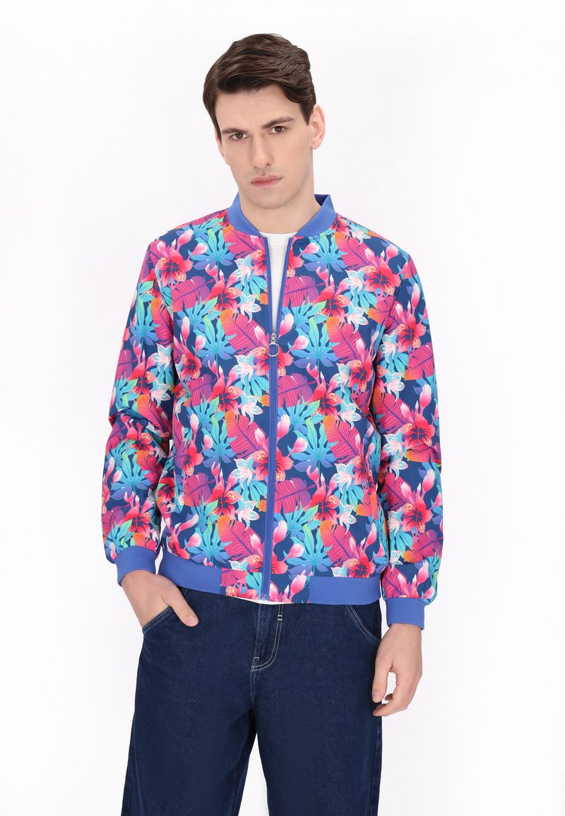 Jachetă de bombă florală cu un model tropical roz și albastru, cu fermoar în față și manșete și tiv din material elastic. Asortată cu pantaloni de blugi închisi la culoare.