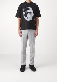 Black cotton t-shirt with a large grayscale graphic on the front, paired with light gray tailored pants and black sneakers.