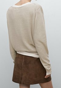 Beżowa bluzka z długim rękawem i szerokim dekoltem, noszona na białej bluzce. Brązowa mini spódnica zamszowa z bocznym szwem. Miękkie faktury.