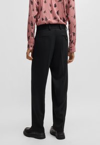 Black trousers with a straight cut, textured fabric, and rear pockets, paired with a pink patterned shirt featuring black abstract designs.