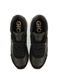 Zapatilla negra con parte superior de cuero liso, acentos de ante texturizado, tres ojales para los cordones y detalles del logo dorado en la lengüeta.