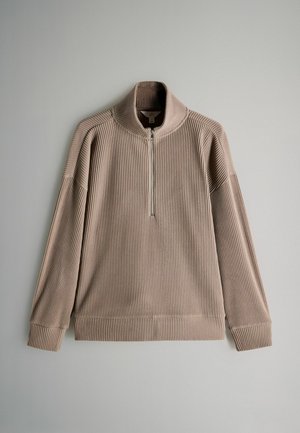 Beżowy sweter z prążkowanej tkaniny, z kołnierzem na suwak do połowy, posiadający długie rękawy i luźny krój. Tekstura jest miękka i lekko elastyczna.
