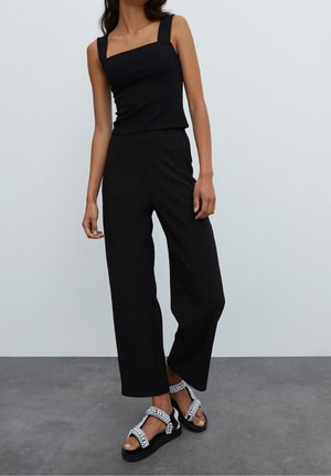 Woman wearing a black square-neck sleeveless top, wide-leg black pants, and black platform sandals with silver embellishments.