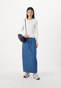 Maglia a maniche lunghe bianca a coste abbinata a una lunga gonna di jeans blu. Indossata con sneakers metalliche e una piccola borsa nera. Design semplice.