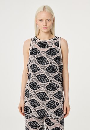 Vrouw met recht blond haar, gekleed in een mouwloos roze en zwart gebreid bovenstuk en broek met een herhalend vispatroon.