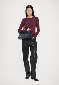 Langärmliges burgunderfarbenes Oberteil, schwarze Lederhosen und schwarze Ballerinas. Trägt eine marineblaue Handtasche mit einem Schlüsselanhänger-Akzent. Minimalistisches Design.