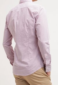 Camisa de manga larga con un pequeño patrón de cuadros rojos y blancos, diseño ajustado, puños con botones y una tabla en la parte trasera para mayor movilidad.