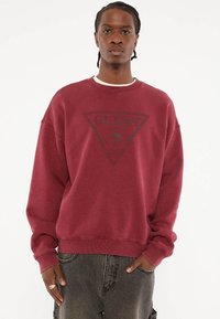 Bordeaux sweatshirt met een ronde hals, voorzien van een zwart driehoekig logoontwerp in het midden. Zacht, textuurstof met geribde manchetten.