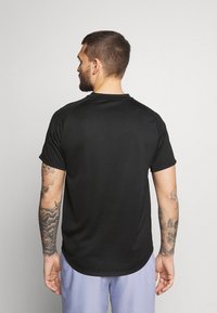 Camiseta deportiva negra de manga corta, con un cuello redondo y una textura suave. La parte posterior presenta un diseño limpio sin logotipos.