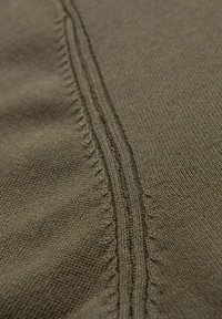 Tissu olive avec un tissage texturé, présentant des coutures visibles le long d'une couture centrale et des détails subtils en tricot fin.